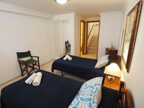 Una camera d'albergo con due letti singoli, una sedia, un tavolino con una lampada e una scala che conduce a un piano superiore.