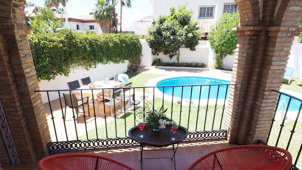 A patio with two red wicker chairs, a small table with a plant, and a swimming pool in the background. - Nerja Paradise Rentals - Villa Victoria (Nerja)