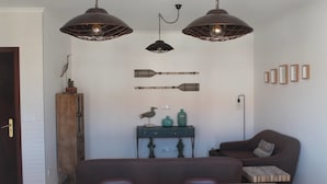 A dining area with a wooden table, two pendant lights, a wooden cabinet, and a sofa. - Guilhim Guest House (Nazaré)
