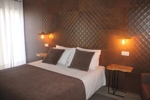 A neatly made bed with a brown blanket, two bedside tables with lamps, and a quilted wall pattern. - Guilhim Guest House (Nazaré)