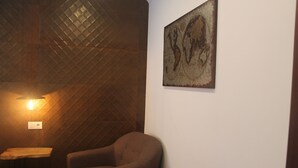 A room with a wooden textured wall, a single brown armchair, a small wooden table, and a wall-mounted artwork. - Guilhim Guest House (Nazaré)