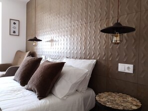 A modern bedroom with a textured wall, a bed with white and brown bedding, two pendant lights, and a small round table with wooden objects. - Guilhim Guest House (Nazaré)