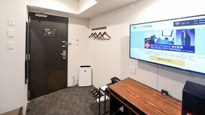 A hotel room with a wooden table, a projector screen displaying a hotel advertisement, a door with a lock, and a small air conditioning unit. - Hotel Livemax Asakusa Ekimae (Tokyo)