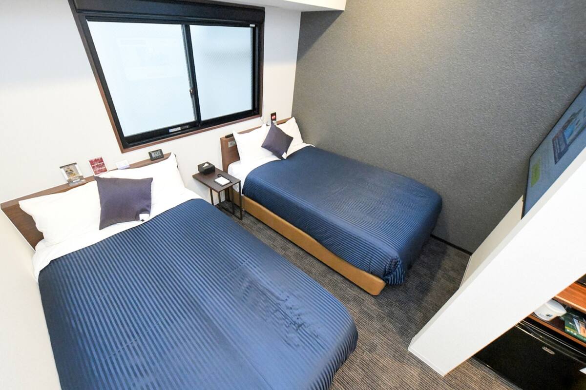 A twin room with two beds, a small bedside table, a nightstand, a window, and a view of the sky.