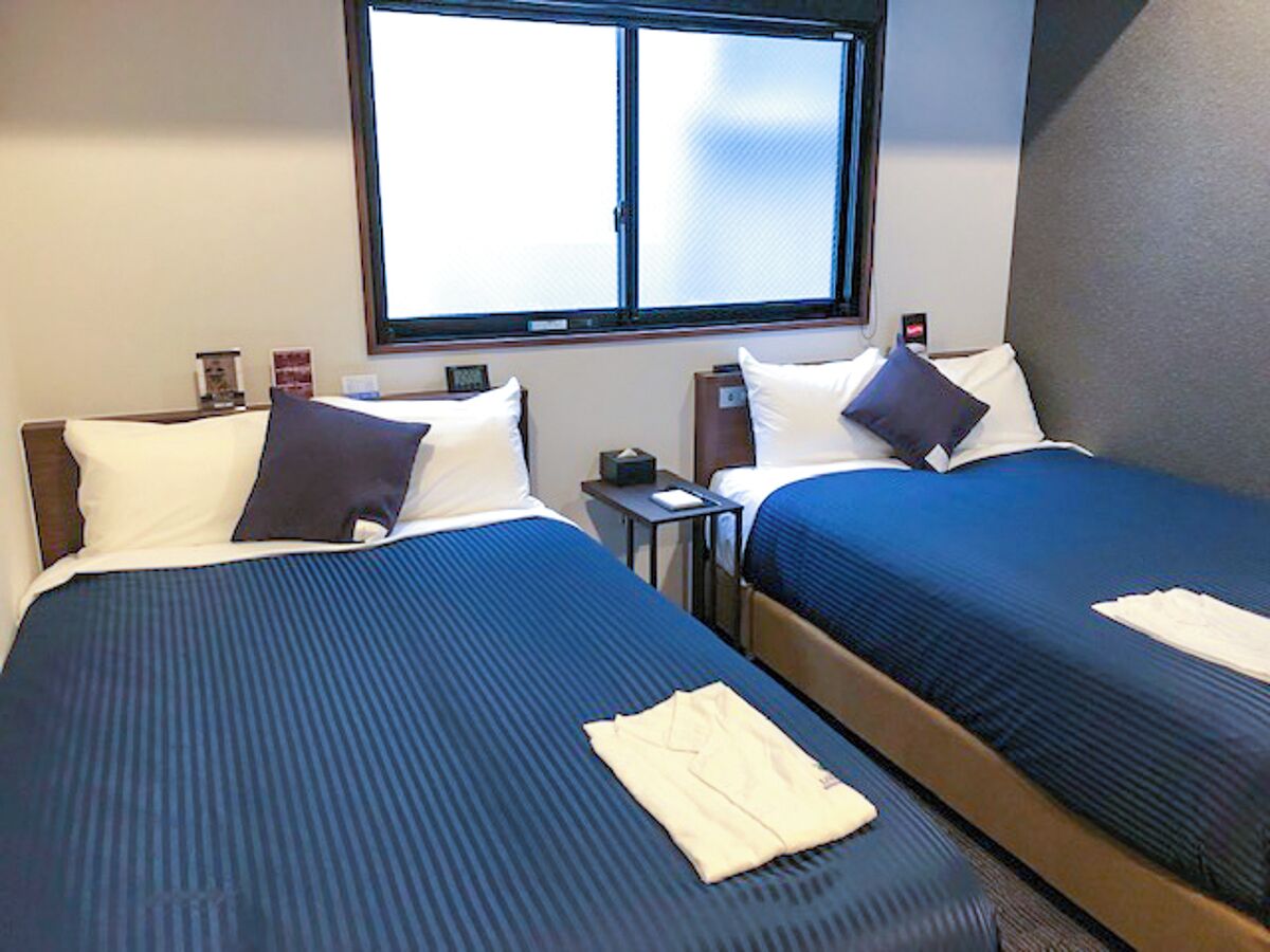 Habitación de hotel con dos camas, una ventana, una mesita de noche y una pequeña mesa.