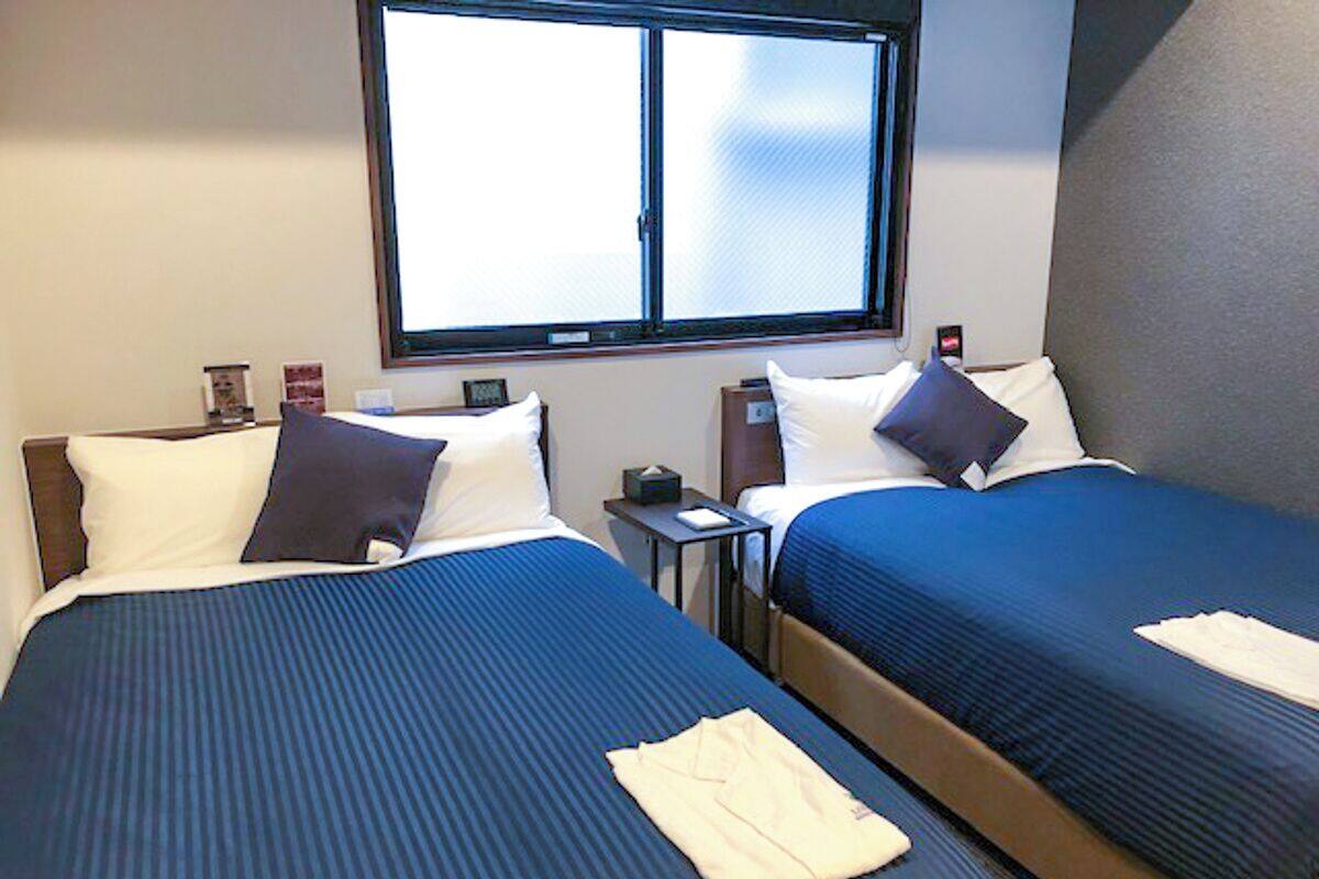 A hotel room with two beds, a window, a nightstand, and a small table.