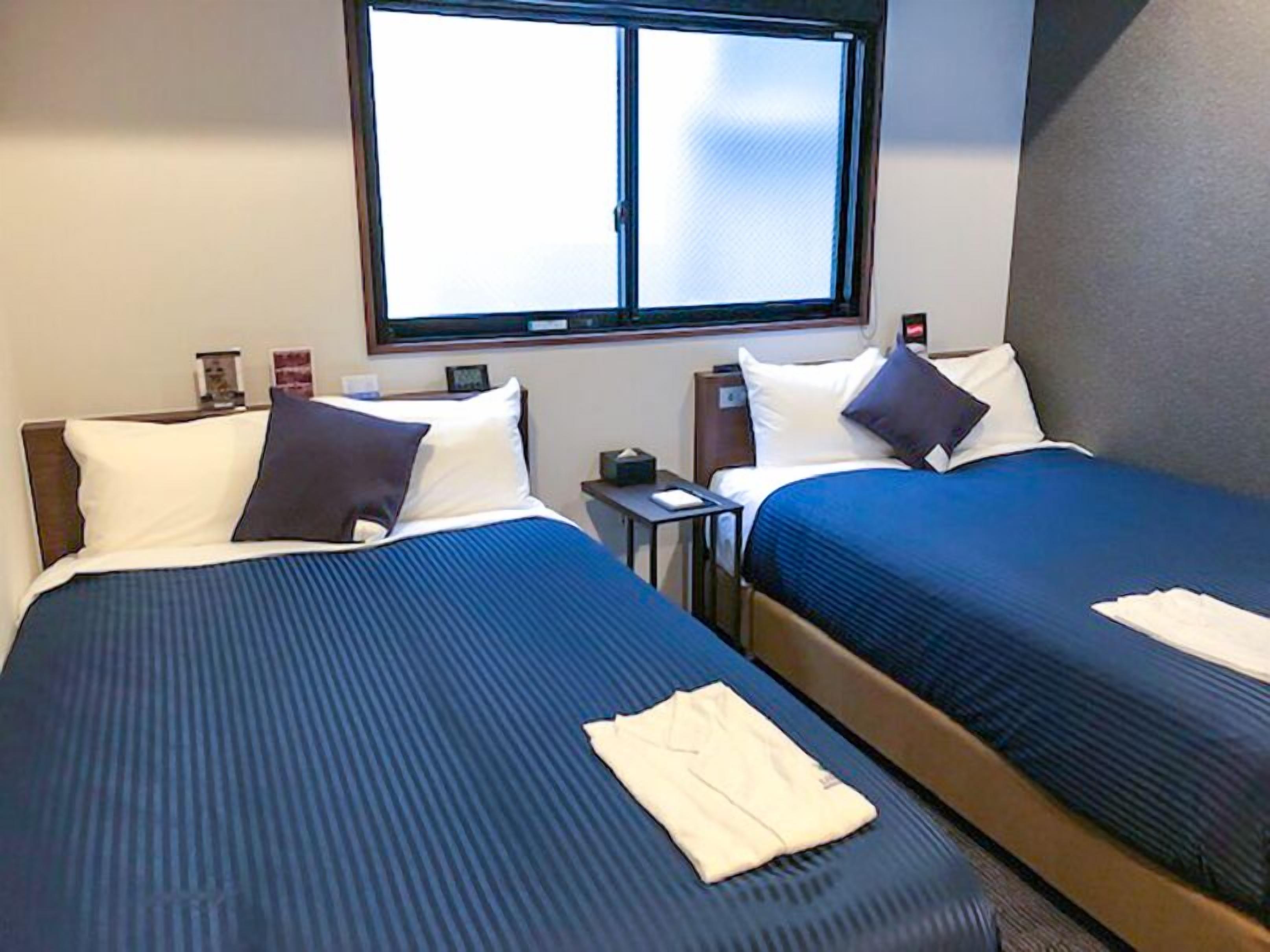 Une chambre d’hôtel avec deux lits, une fenêtre, une table de chevet et une petite table.