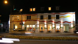 Ein Gebäude mit einer markanten, gewellten Fassadengestaltung, zahlreichen Fenstern und einem Eingangsbereich mit Tischen und Stühlen.