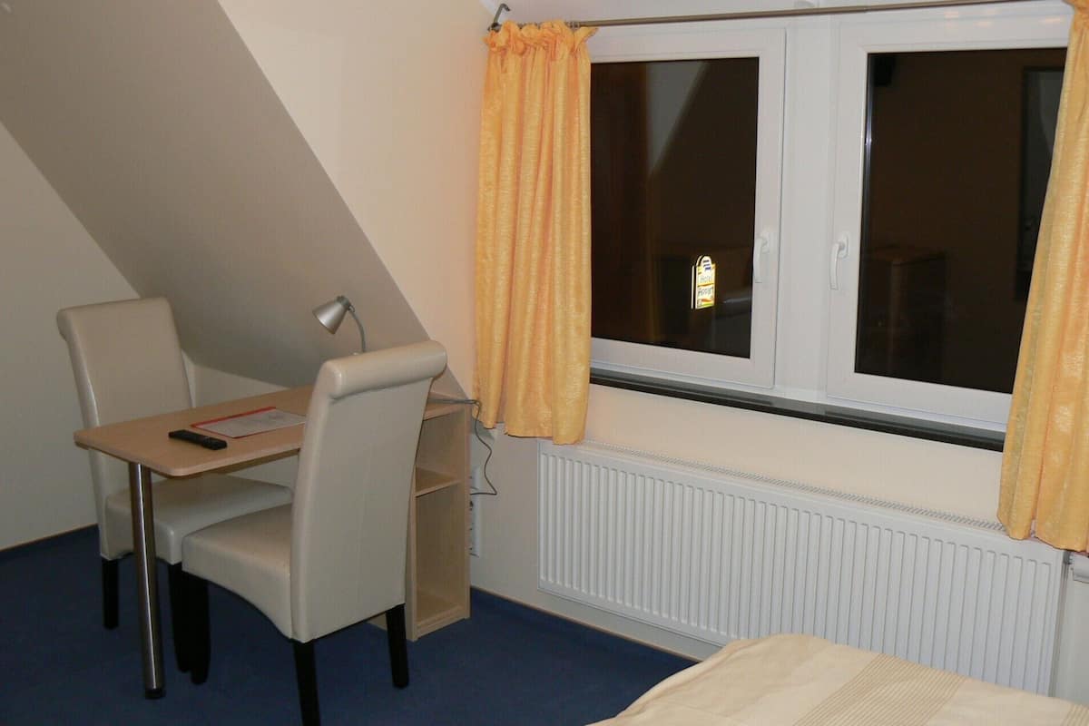 A small, single-room hotel room with a desk, chair, and a window with curtains.