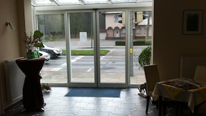 Ein Hotel Eingang mit Glastür, einem Blumentopf, einem Tisch mit gelber Tischdecke und einem gefliesten Boden.