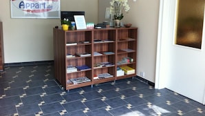 Ein Empfangsbereich mit einem Holzregal, gefüllt mit Zeitschriften und Büchern, einem Schild mit der Aufschrift 'Hotel Appartement.de' und einer Tür mit goldfarbenem Glaspaneel.