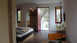 Une chambre à coucher comprenant un lit, un bureau, une chaise, une armoire et une porte-fenêtre coulissante donnant sur un balcon.