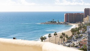 A coastal hotel with a beach view, a rocky breakwater, and palm trees.