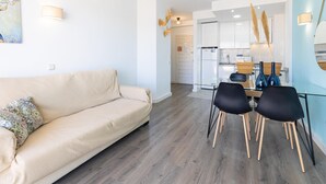 A modern living room with a beige sofa, a dining table with black chairs, and a kitchen in the background.
