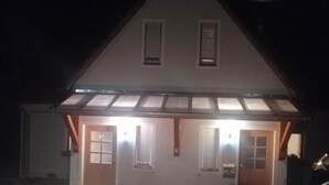 A two-story house with a covered porch, a driveway, and a car parked in the driveway. - Pension Karolingerweg (Lauterhofen)