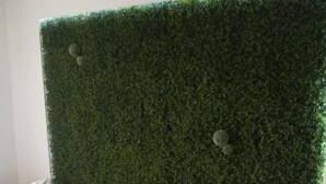 A room with two single beds, each with a wooden frame and a green mattress. There is a white bedside table with a lamp on each bed. The headboard is covered with a green artificial grass wall. - Pension Karolingerweg (Lauterhofen)