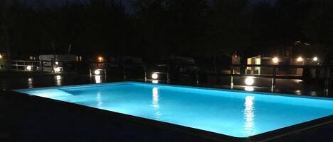 Une piscine rectangulaire à l’eau d’un bleu clair, entourée d’une plage de piscine aux couleurs sombres.