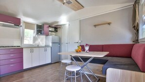 A compact kitchen with a dining area, including a table, two stools, and a red cushioned bench. - Kamp Slapic Mobile Homes (Duga Resa)