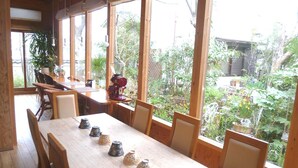 A dining area with a long wooden table, chairs, and a view of a garden through large windows. - Yamashiroya (Nara)