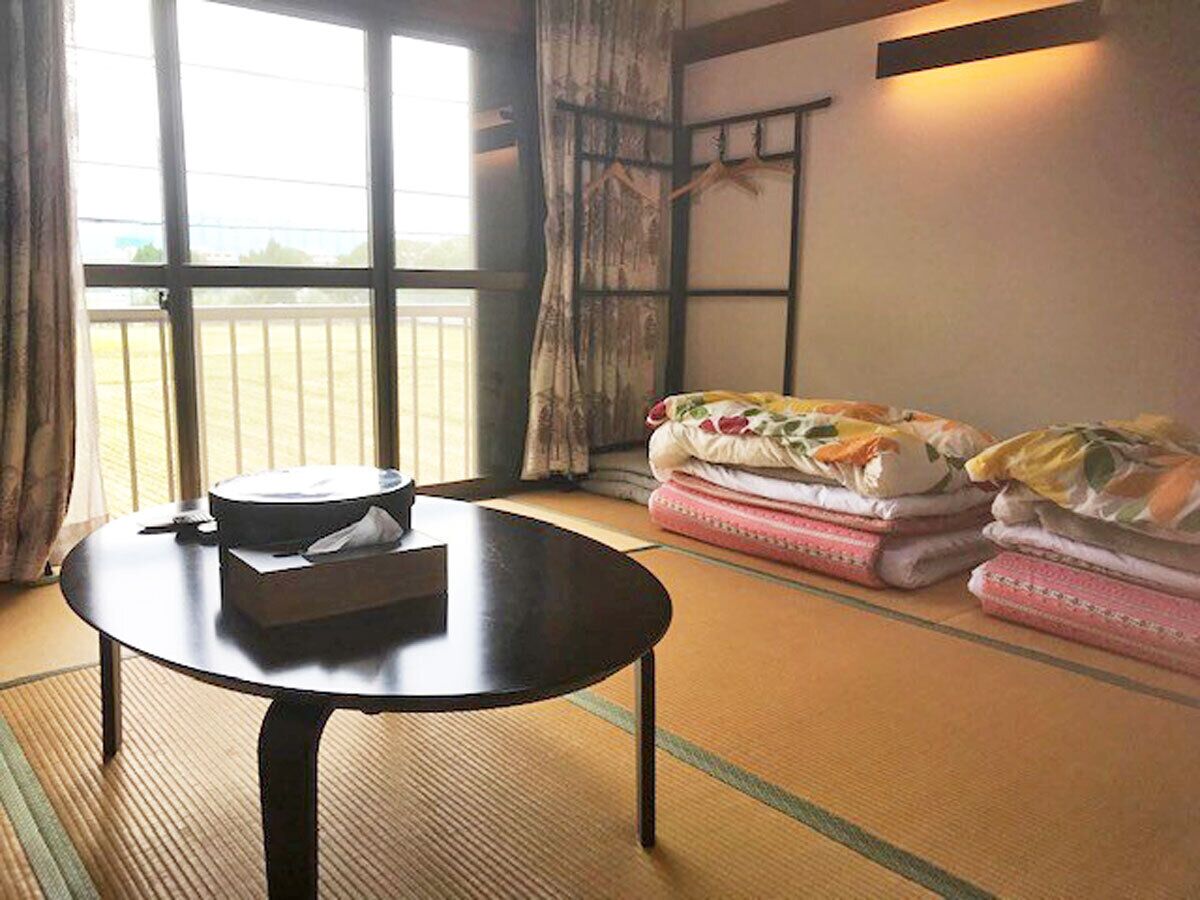 A traditional Japanese room with tatami flooring, a low table with a cushion, and a bed with floral bedding.