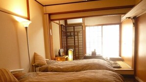 A traditional Japanese-style room with two beds, a desk, and a window with a view of the outside. - Yamashiroya (Nara)