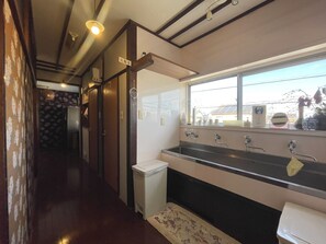 A narrow hallway with a sink and window, wooden doors, and a small trash bin. - Yamashiroya (Nara)