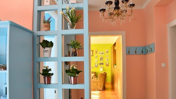 A hallway with a blue shelving unit filled with potted plants, a chandelier, and a wall with a 'JESS' sign. - Apartments Oldtimer (Zagreb)