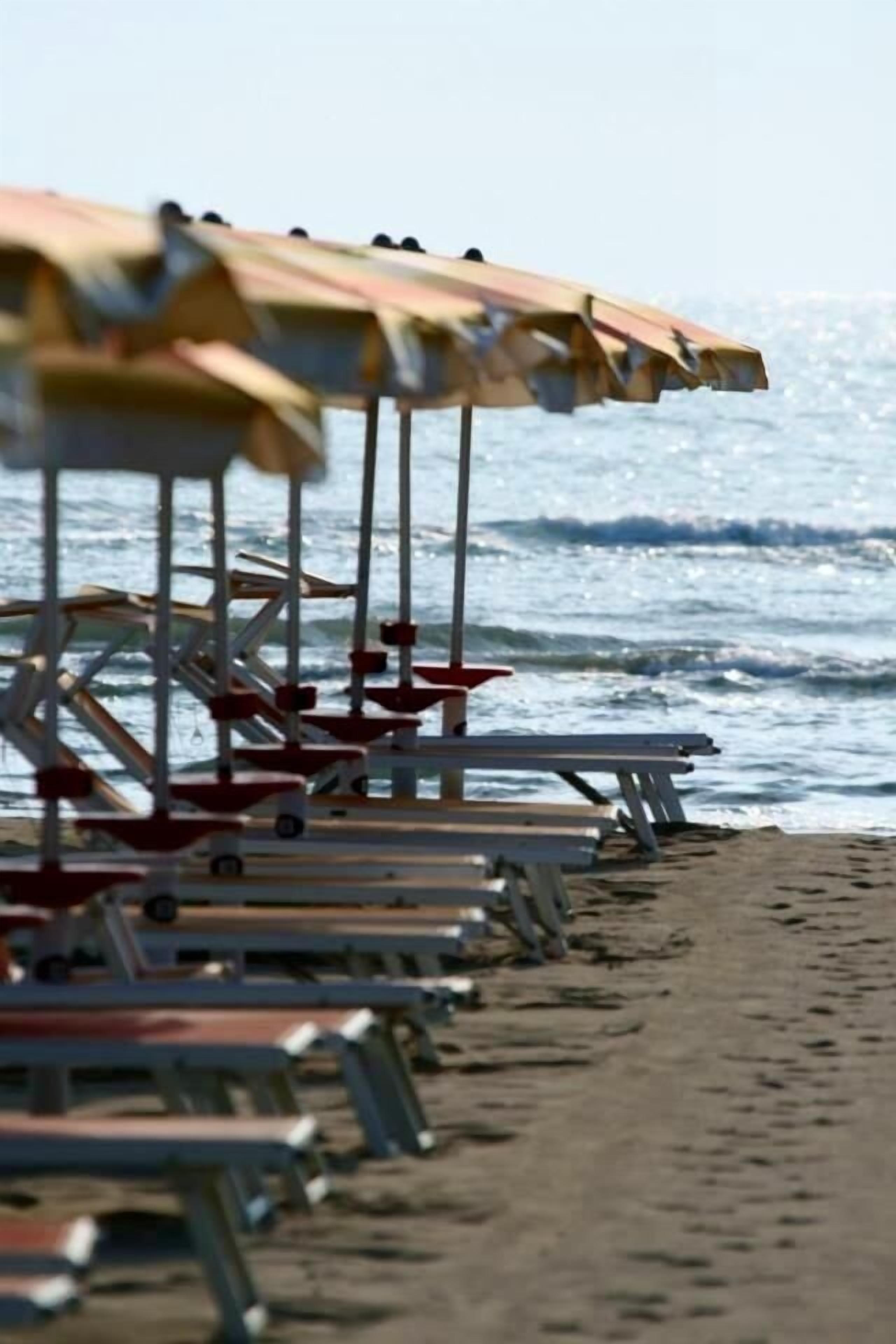 Eine Reihe von Strandsonnenschirmen und Bänken entlang eines sandigen Ufers.