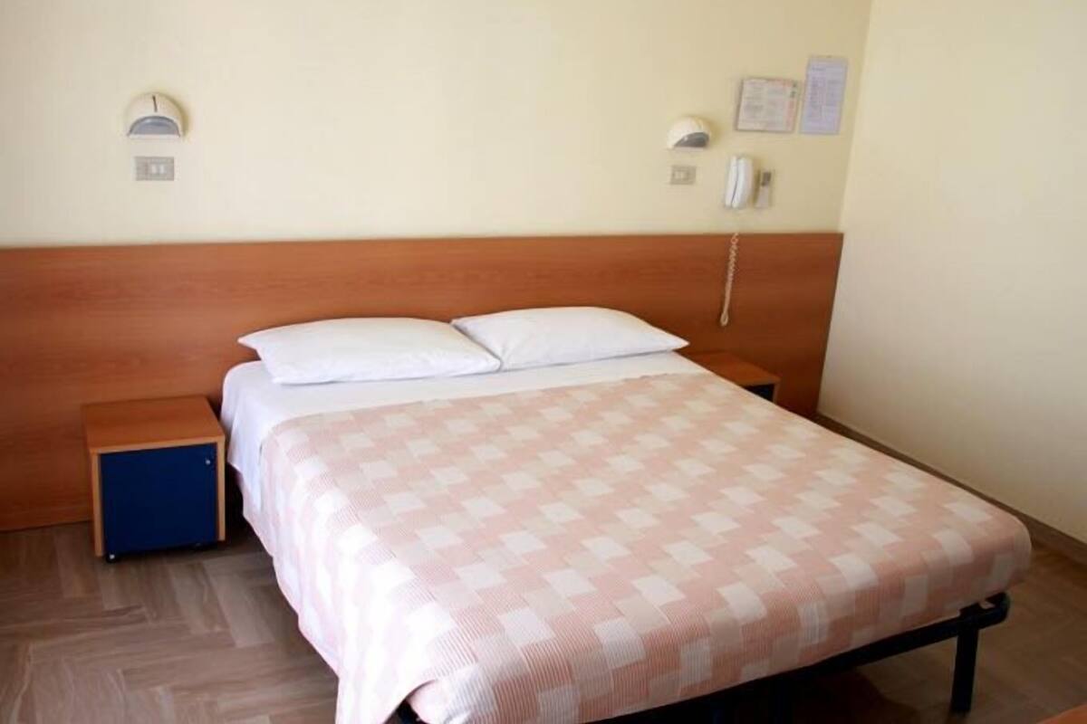 Una cama individual con cabecera de madera, una mesita de noche y un teléfono instalado en la pared.