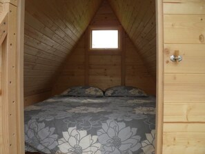 A small, wooden attic bedroom with a single bed, a window, and a door.