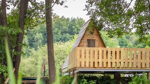 A wooden cabin with a sloped roof, situated in a forested area with trees and greenery around. - Kamp Slapic Glamping (Duga Resa)