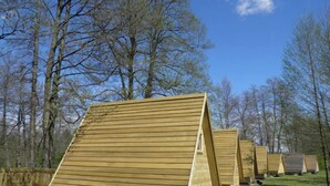 A row of wooden cabins with sloped roofs, set in a forested area. - Kamp Slapic Glamping (Duga Resa)