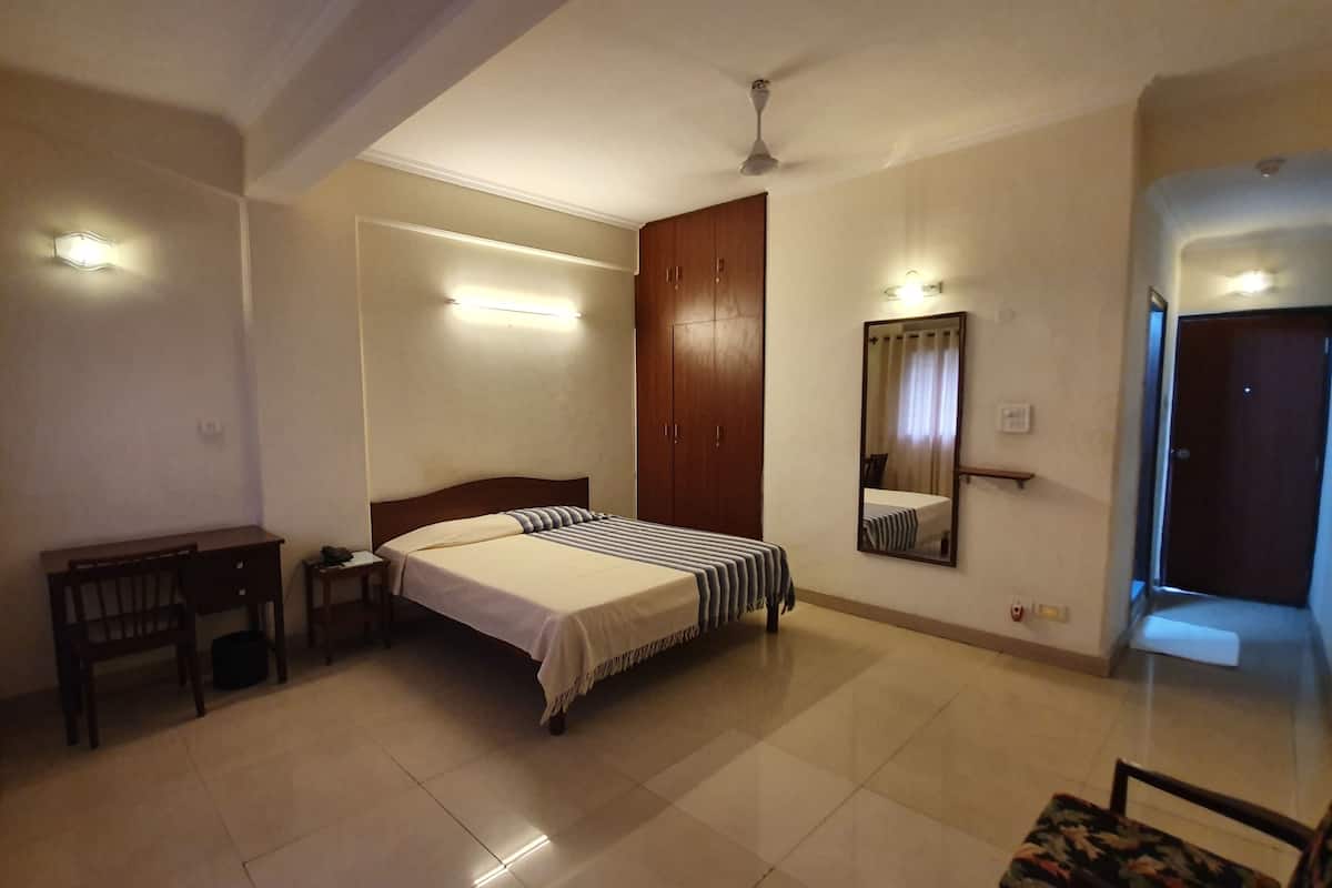 A hotel room with a bed, a desk, a wardrobe, a mirror, and a door.