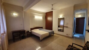 Habitación de hotel con cama, escritorio, armario, espejo y puerta.