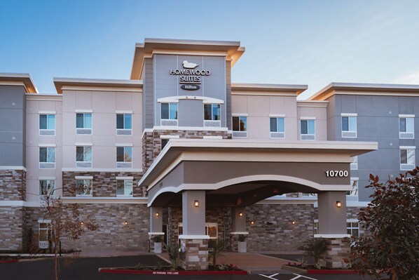 Een meerlaags hotel met een modern ontwerp, met een opvallende entree en een bord met daarop Homewood Suites Hilton.