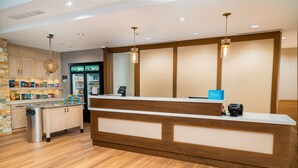 Un espace d’accueil d’hôtel avec un comptoir de réception en bois, un minibar et un bar à collations en libre-service.