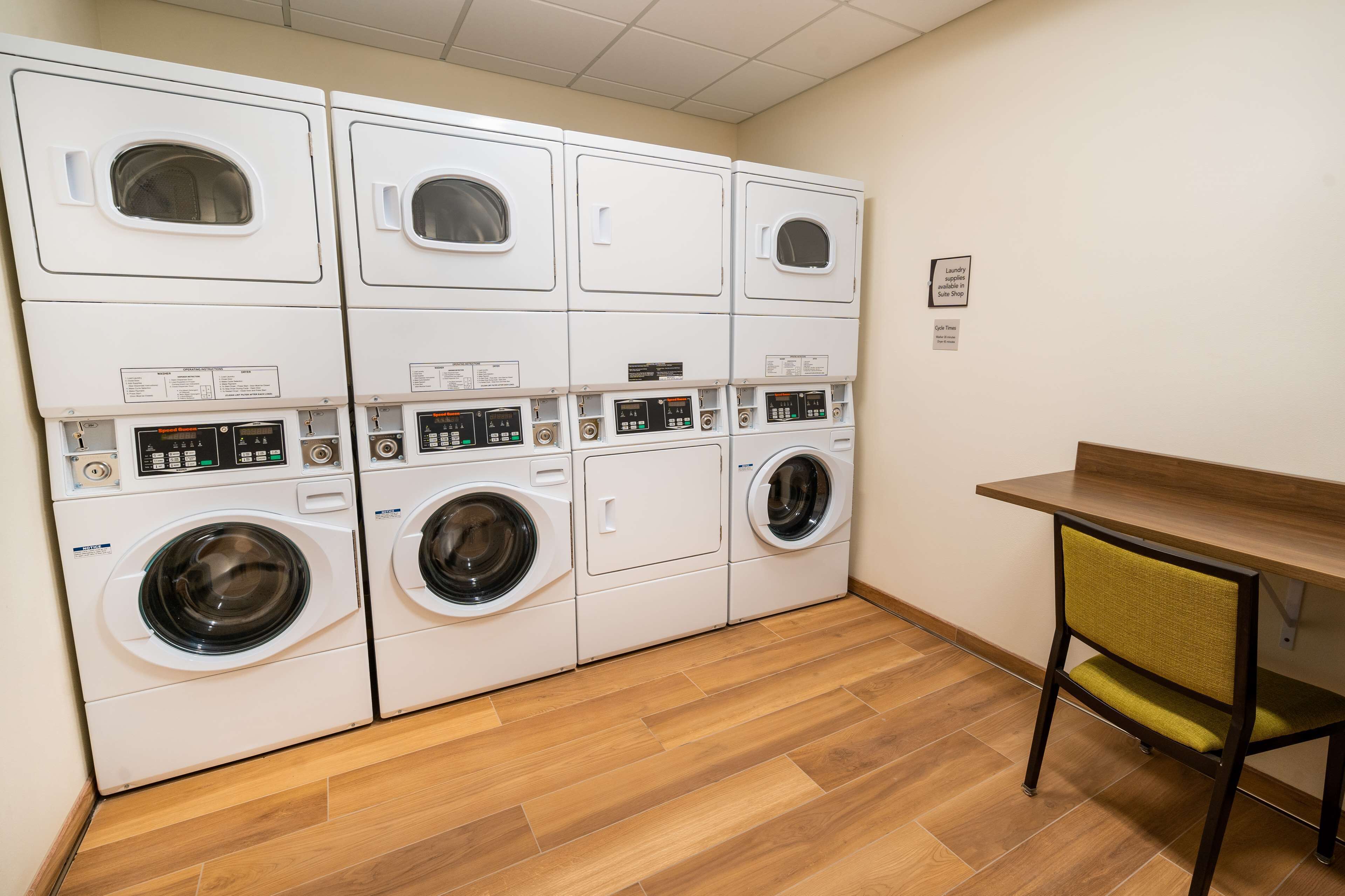 A laundry room with multiple washing machines and dryers, a wooden table, and a chair.