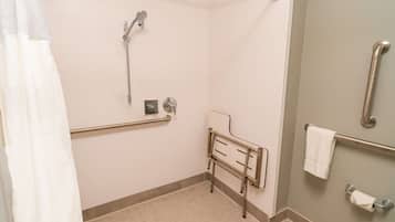 Un baño con ducha, barras de apoyo, secamanos y perchero para toallas.