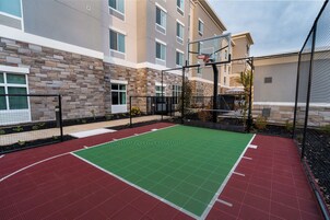 Una cancha de baloncesto al aire libre junto a un edificio con fachada de piedra y varias ventanas.