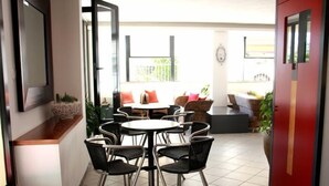 A dining area with round tables and black chairs, a red accent wall, and a view of the outdoor seating area. - Hotel Sedonia (Cervia)