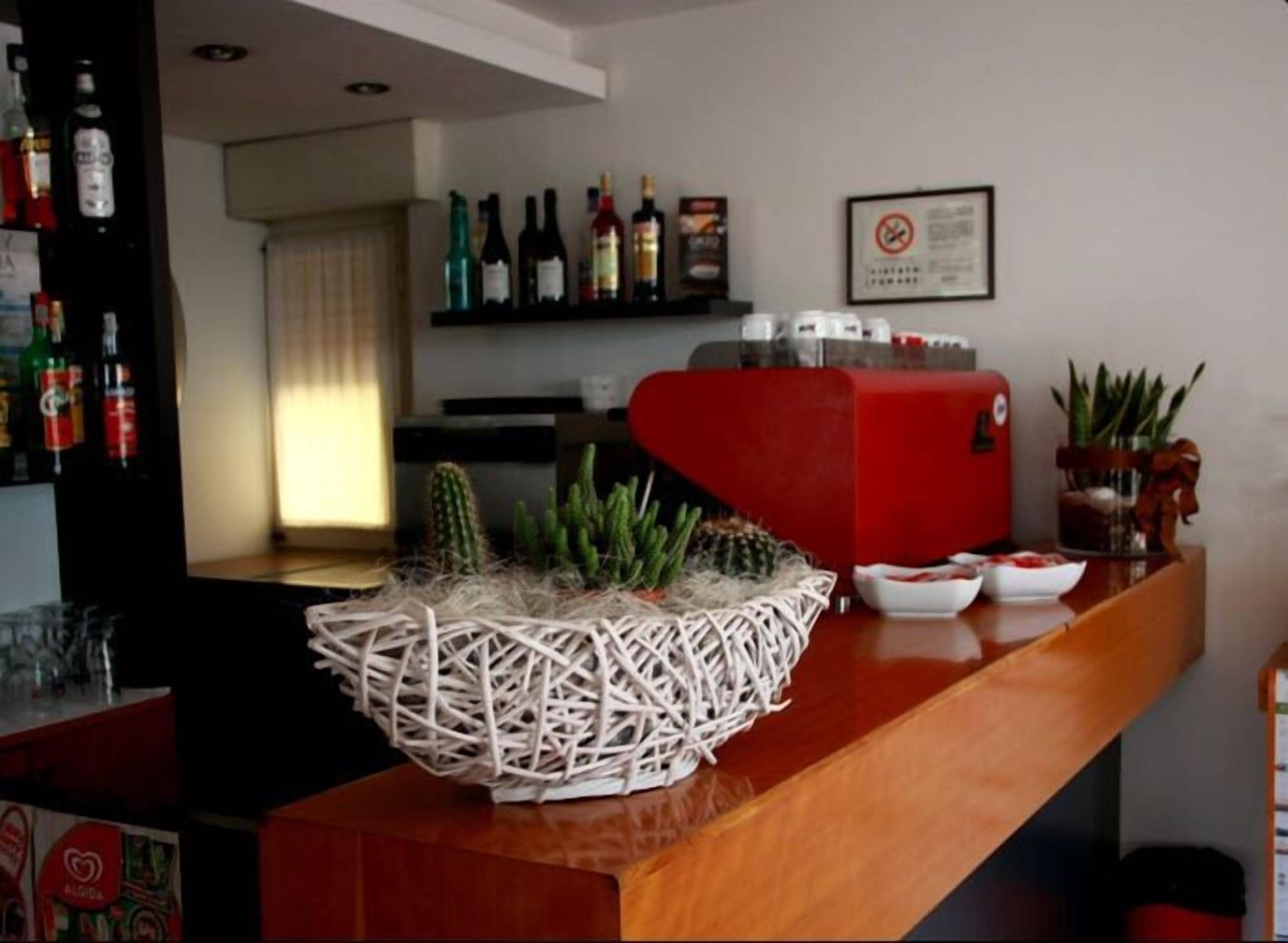 Zona de bar con una cesta de mimbre que contiene plantas, un electrodoméstico rojo y varias botellas en estanterías.