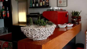 Zona de bar con una cesta de mimbre que contiene plantas, un electrodoméstico rojo y varias botellas en estanterías.