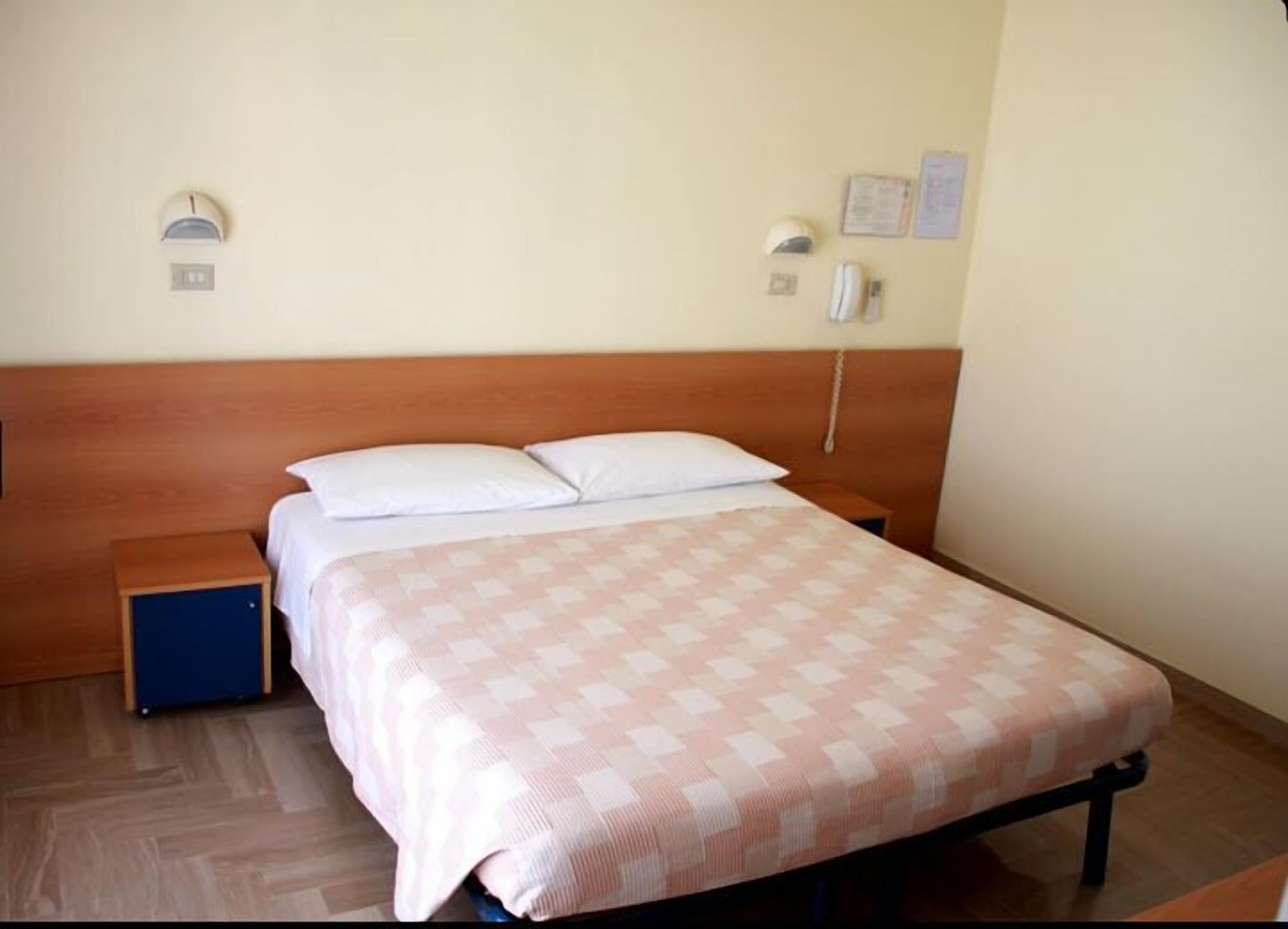 Habitación individual con una cama de madera, mesita de noche, pequeño armario azul y colcha estampada.