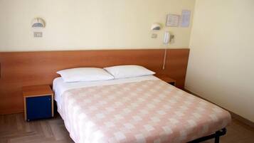 Habitación individual con una cama de madera, mesita de noche, pequeño armario azul y colcha estampada.