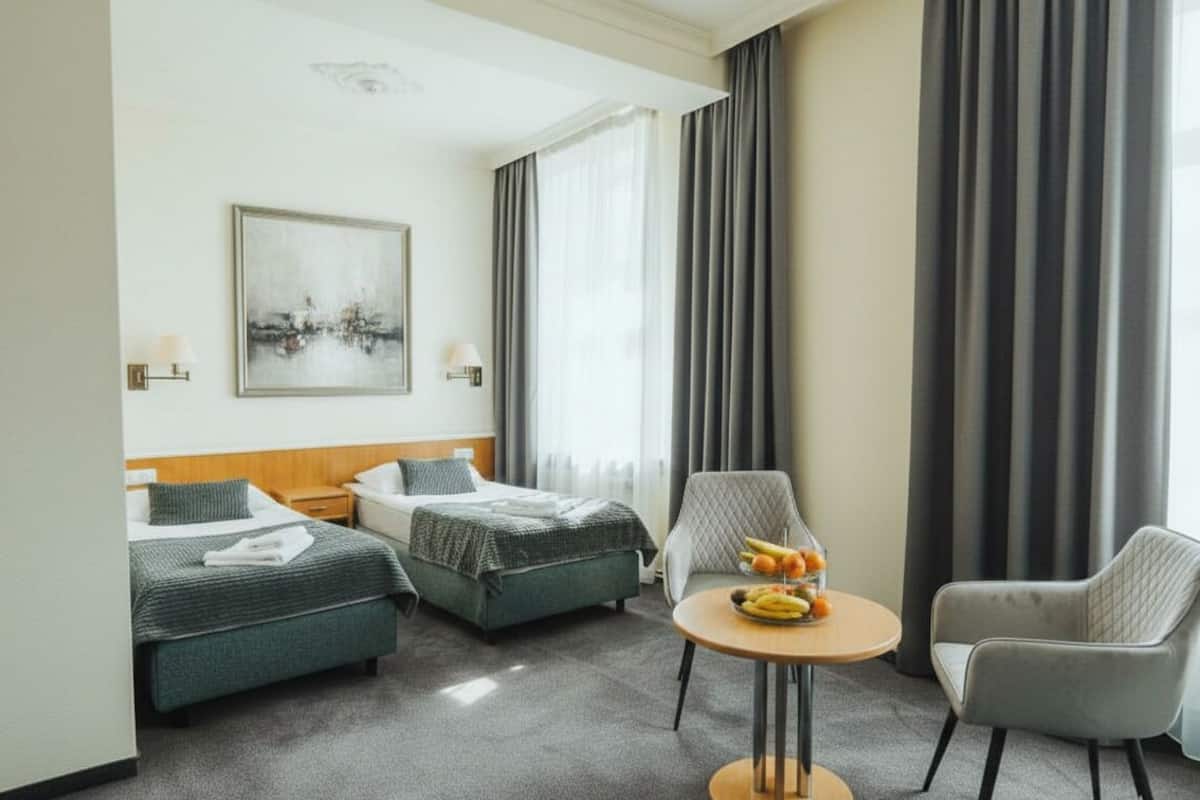 Hotellihuone, jossa on kaksi erillistä sänkyä, pieni pyöreä pöytä, jossa on hedelmiä, tuoli ja taulu seinällä.