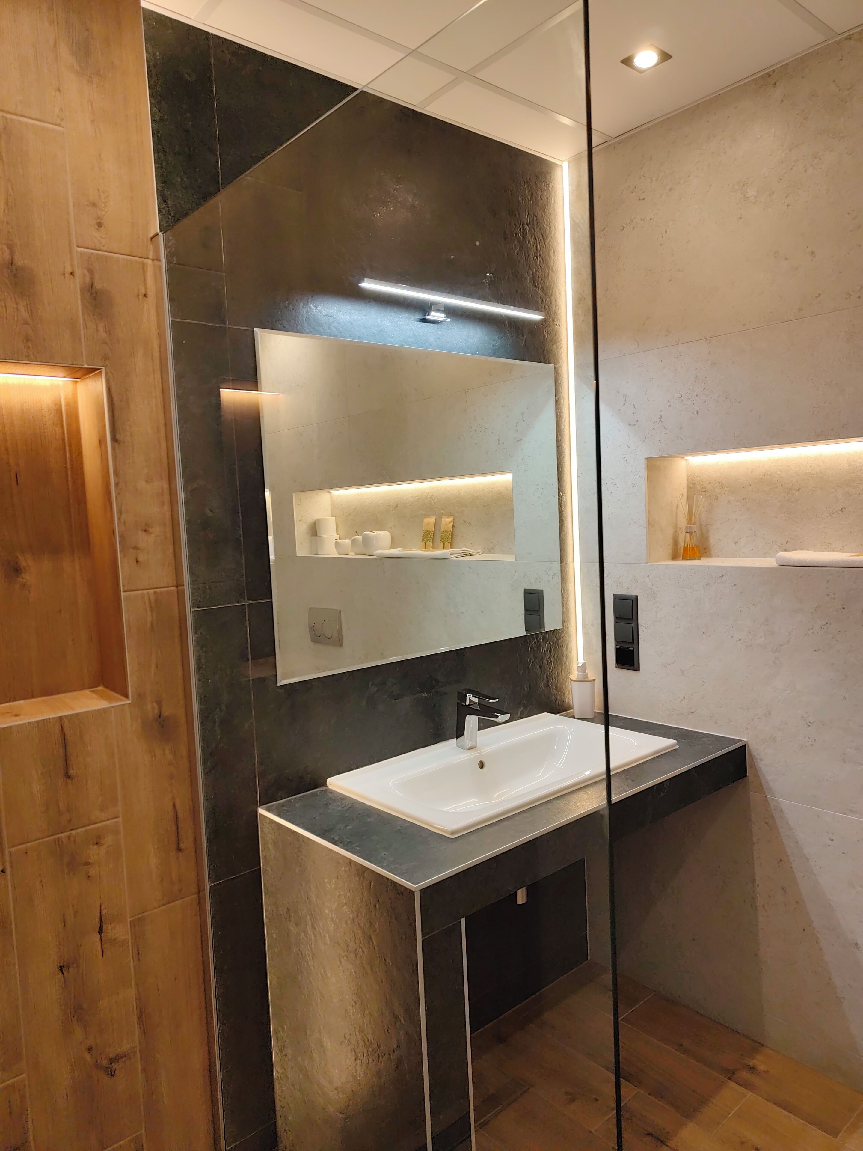 A modern bathroom with a large mirror, a white sink, and a wooden vanity.