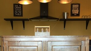 Une cuisine avec des meubles en bois, deux tabourets de bar noirs et des luminaires suspendus.