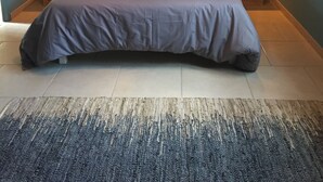 Une chambre avec un grand lit, deux tables de chevet, un luminaire suspendu et un tableau accroché au mur.