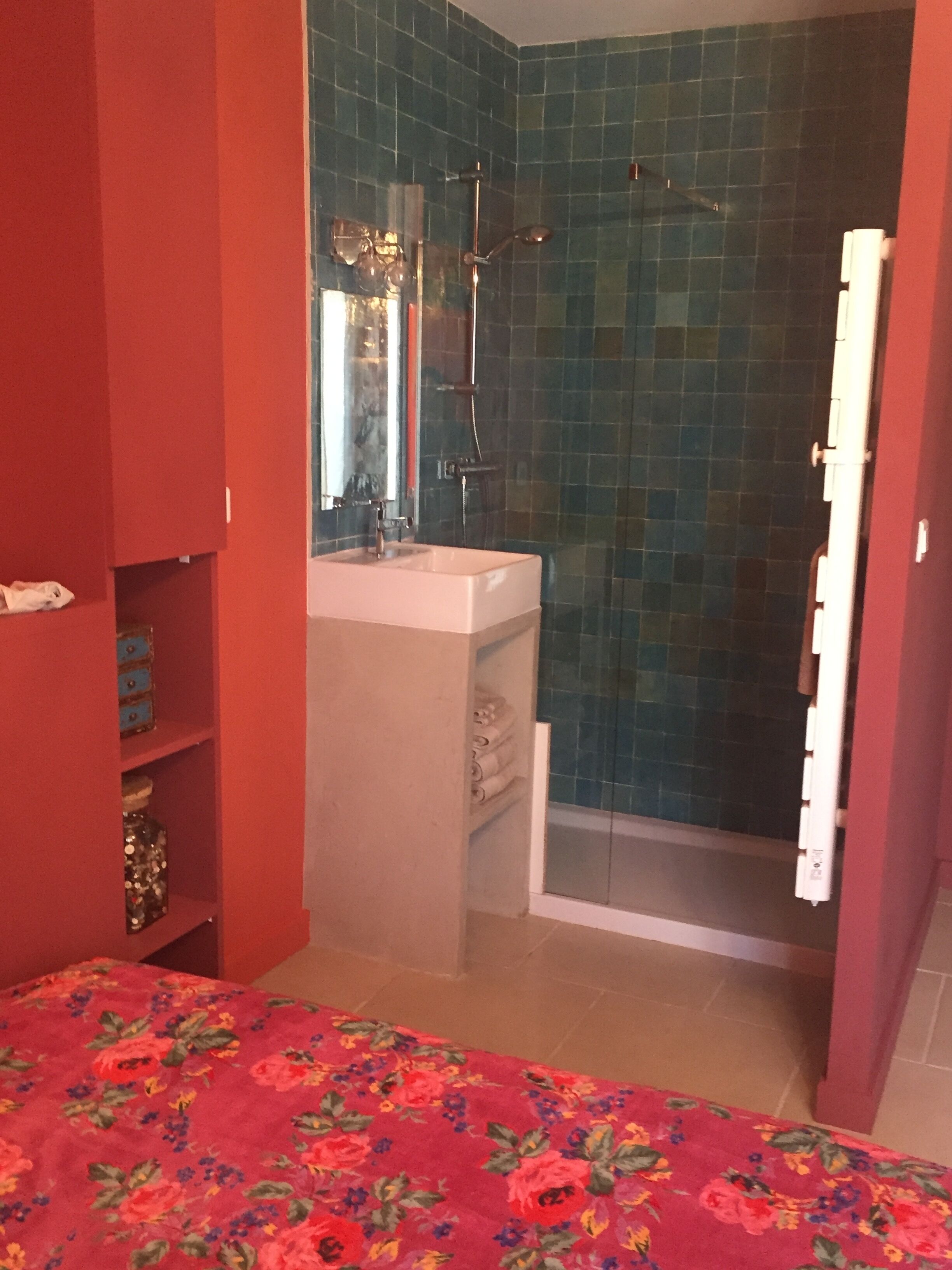 Ein Badezimmer mit Dusche, Waschbecken und Spiegel. Die Wand ist rot und rechts befindet sich eine Tür.