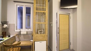 A compact kitchen with a wooden cabinet, a refrigerator, a window, and a television mounted on the wall. - 101 # 1 BR Studio Apartment for solo traveler in Ubud (Ubud)
